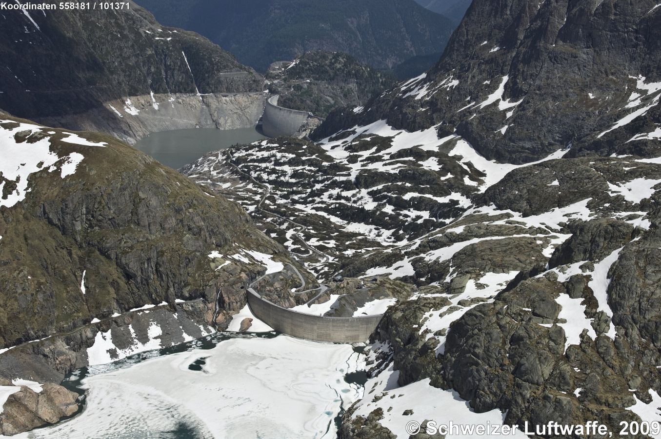 Vieux Emosson (Nant de Drance, VS; Position: 2'560'778.94, 1'101'930.71). Eisbedeckt im Vordergrund: Lac du Vieux Emosson, daraus fliesst der Fluss Nant de Drance. Im Hintergrund (halb leer): Lac d'Emosson. Bergwand oben rechts gehört zu Frankreich. Norden gegen den untern linken Bildrand.